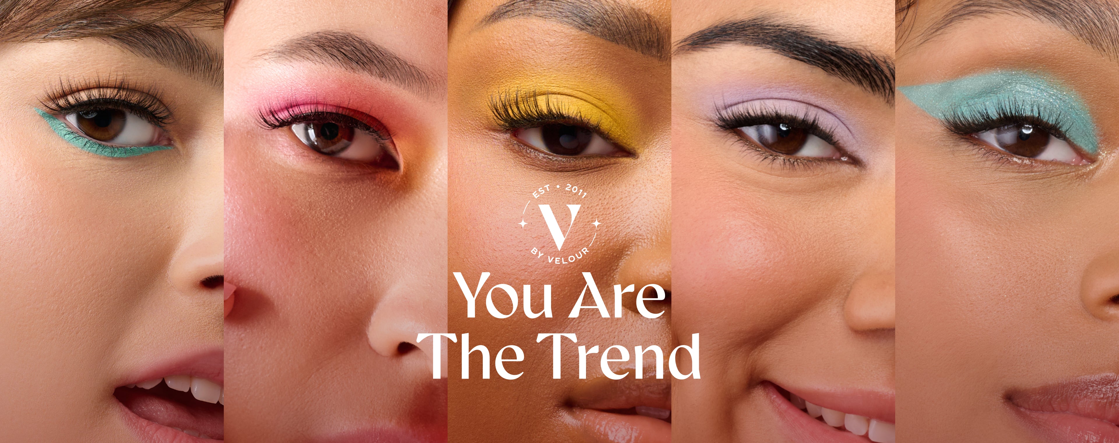 Banner features a close-up of three diverse models' eyes, each showcasing bold, colorful eye makeup and long, voluminous lashes. The left model has teal eyeliner, the middle model wears pink and red eyeshadow, and the right model has yellow eyeshadow, all enhancing their natural beauty. Centered in the image is the V by Velour logo, with the text "You Are The Trend" displayed prominently in elegant, modern typography. The image embodies inclusivity, beauty, and self-expression.